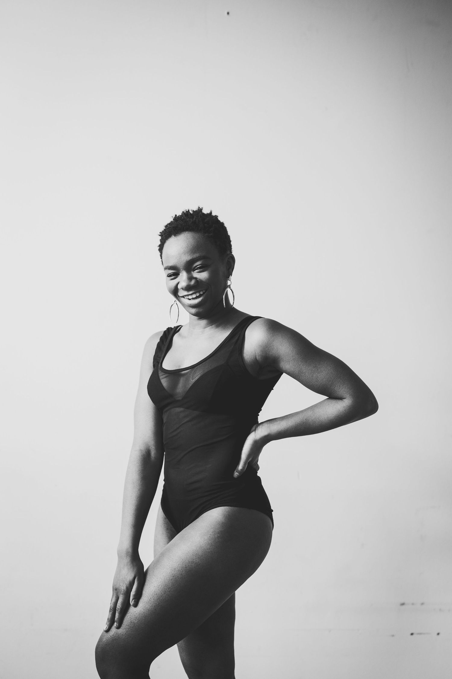Black and white photo of a smiling woman in a swimsuit posing confidently against a light background.