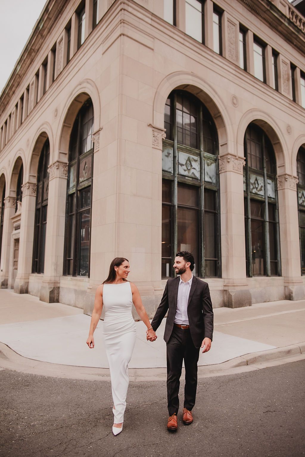 A couple walks together outside a beige stone building with arched windows and architectural details.