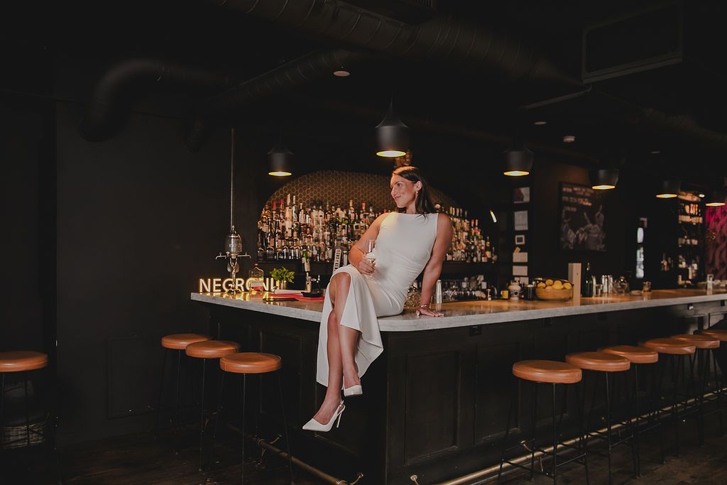 Moody bar scene with atmospheric lighting and wooden bar stools in dark tones.