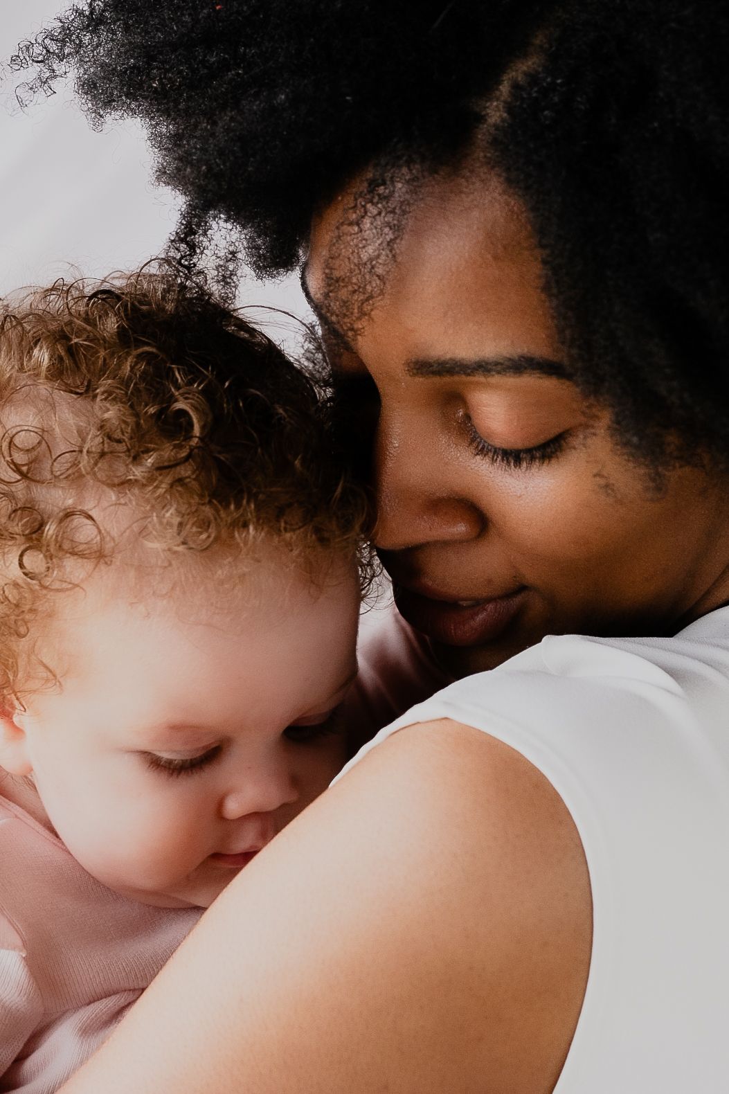 A tender moment shows a parent and child with curly hair sharing a loving embrace against a white background.