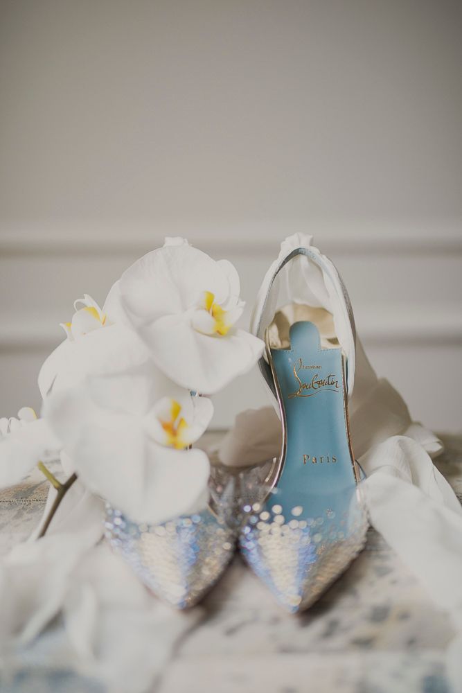 Elegant bridal shoes with delicate blue soles and white orchids arranged on a light background.