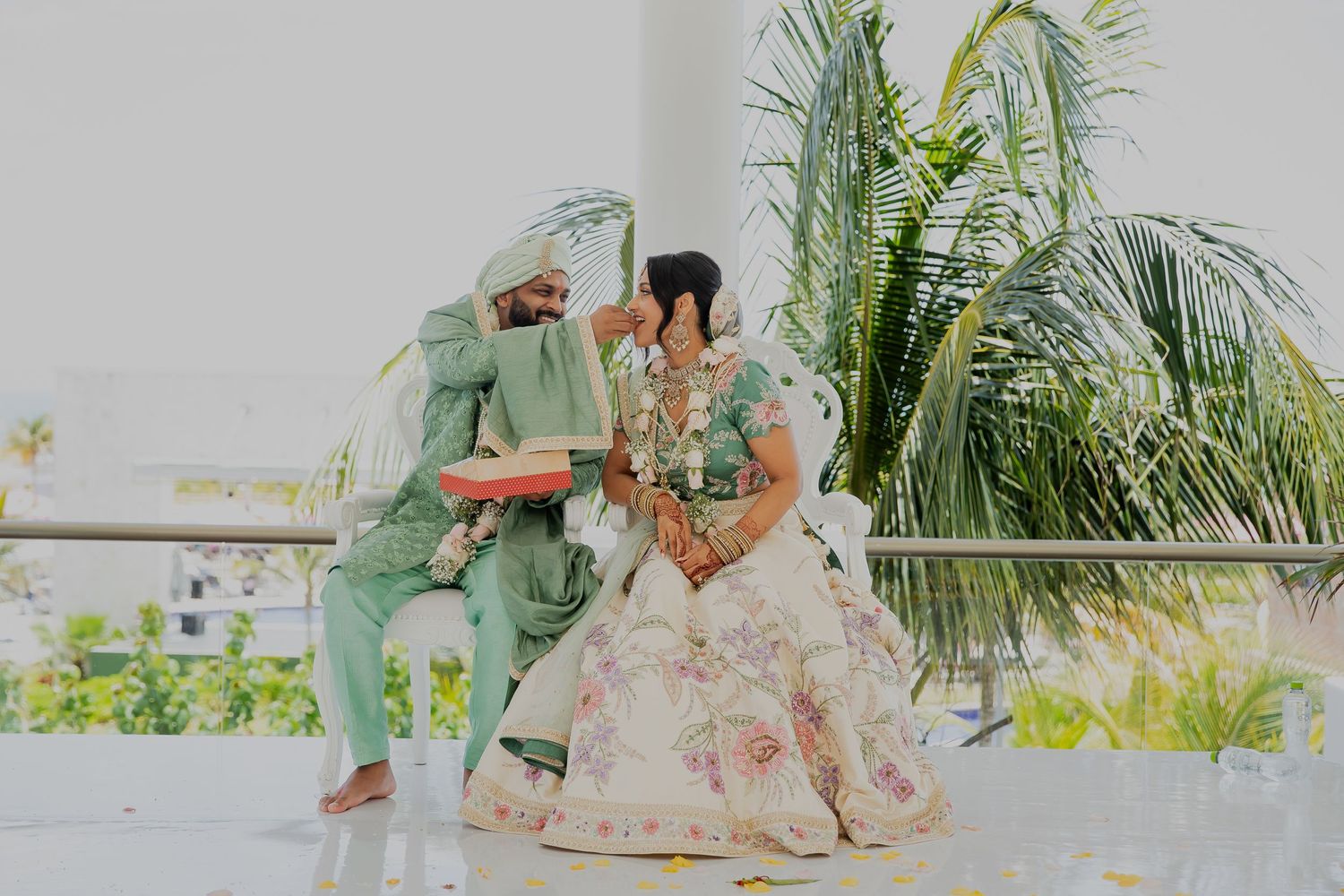 Couple sits together on an outdoor terrace with palm trees in the background.