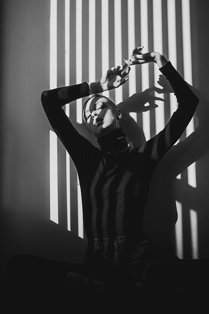 Silhouetted figure against striped window light creating dramatic shadows and patterns.