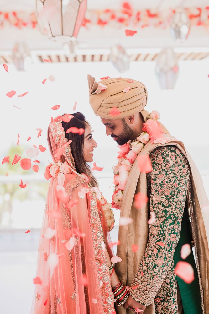A couple in traditional South Asian wedding attire with emerald green and gold embroidered outfits share intimate moments.