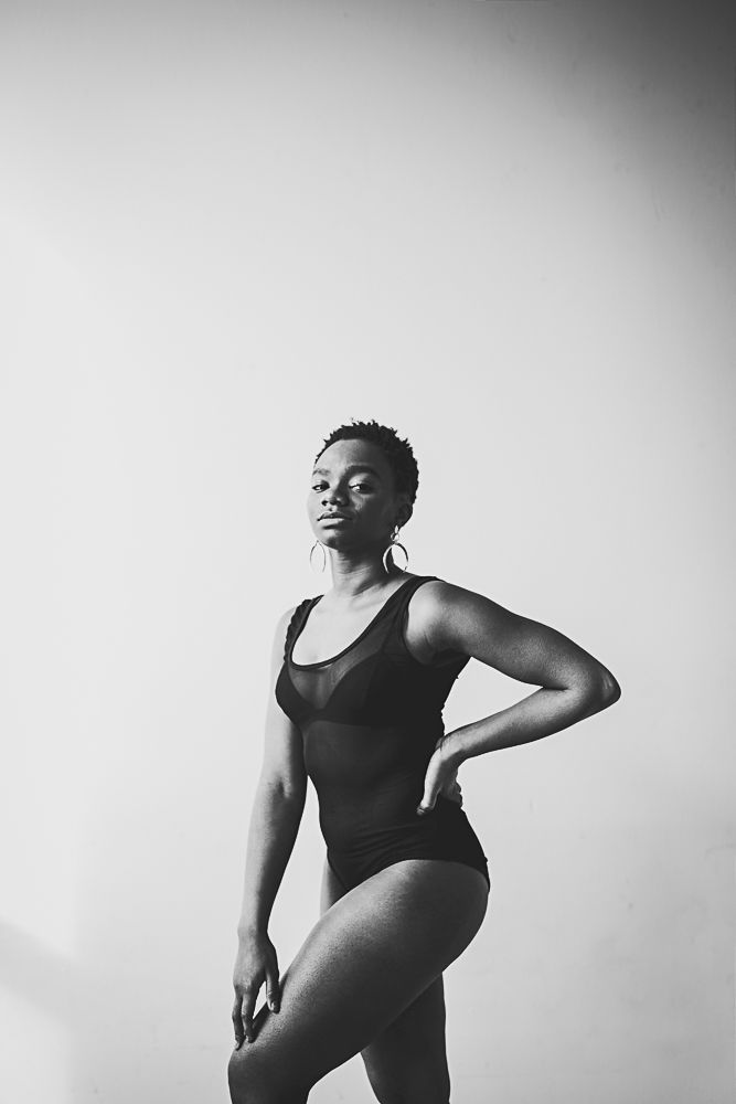 Black and white artistic portrait of a dancer in a leotard striking a powerful pose against a light background.