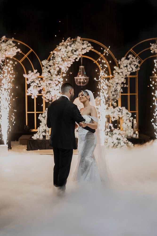 Romantic first dance sequence under illuminated white floral arches with ethereal fog on the dance floor.