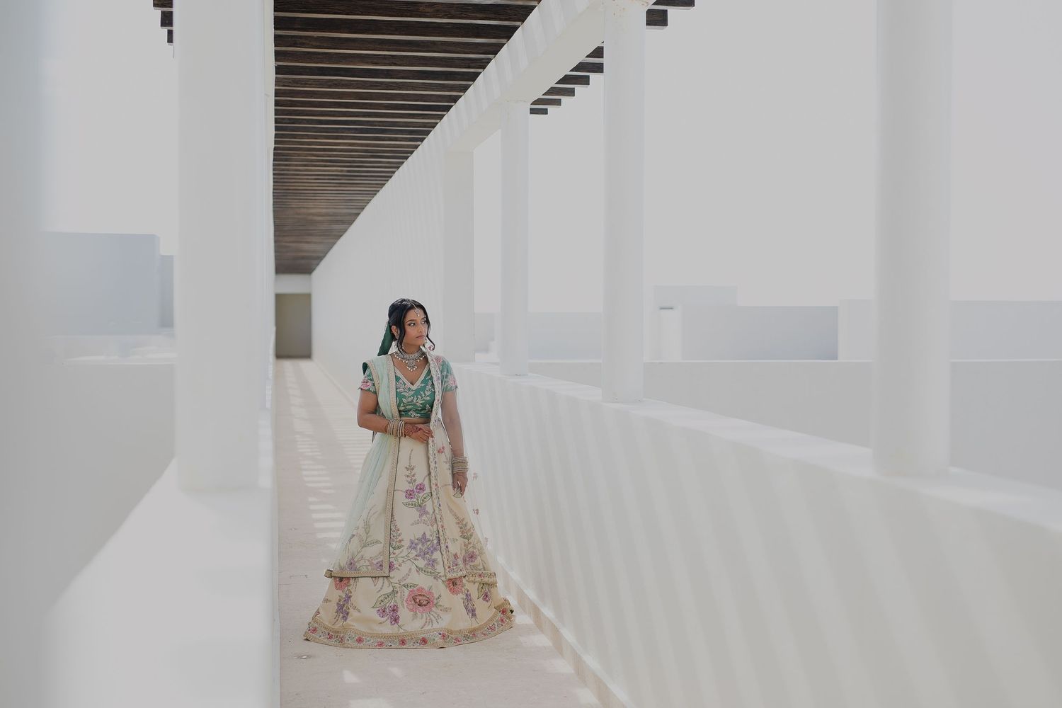 A couple in traditional attire poses against geometric white walls and wooden beams.