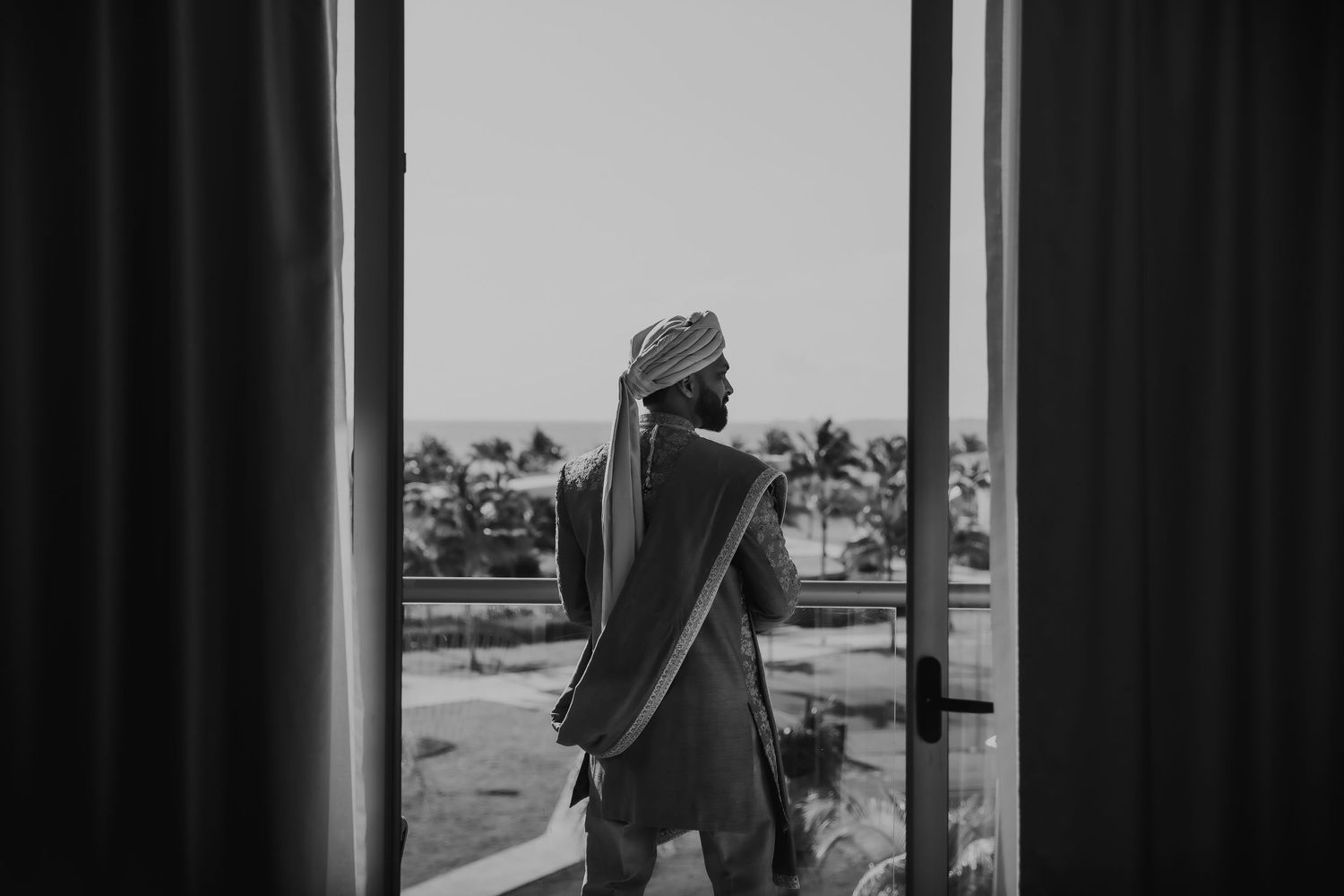 Silhouette of person standing by window with palm trees visible outside.