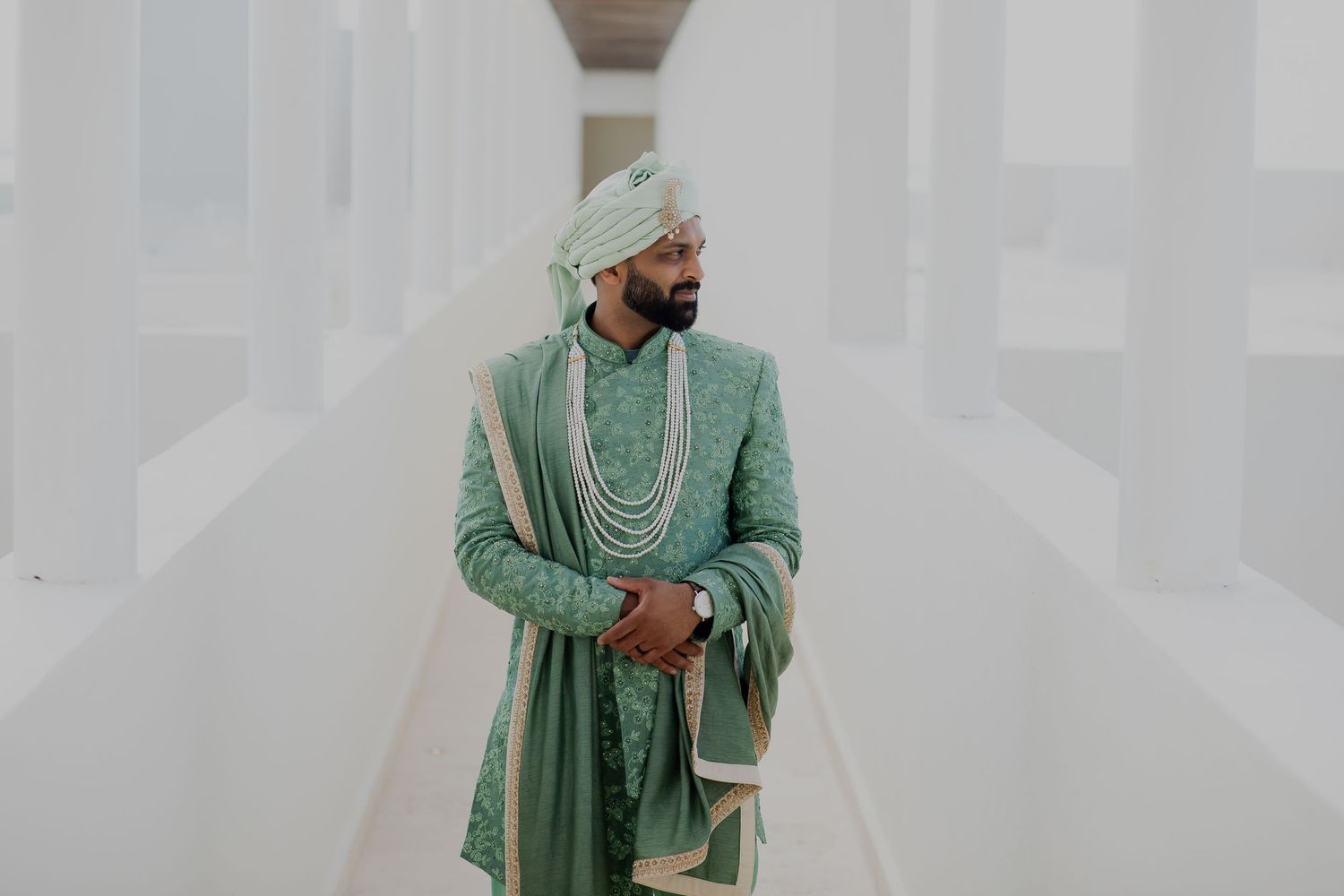 A couple in traditional attire walking through a modern white architectural hallway.