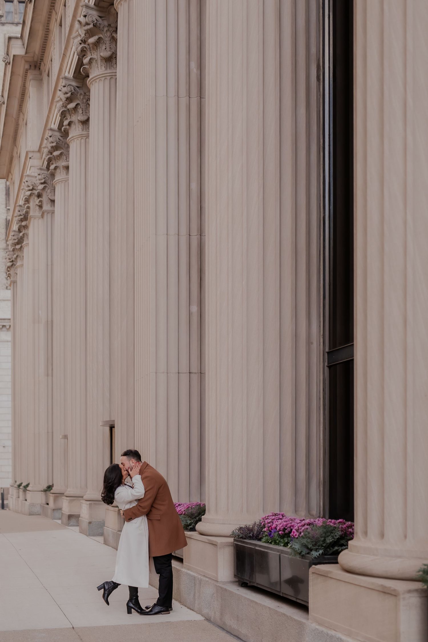 A person sits alone on stone steps between elegant white columns with pink flowers in the background.