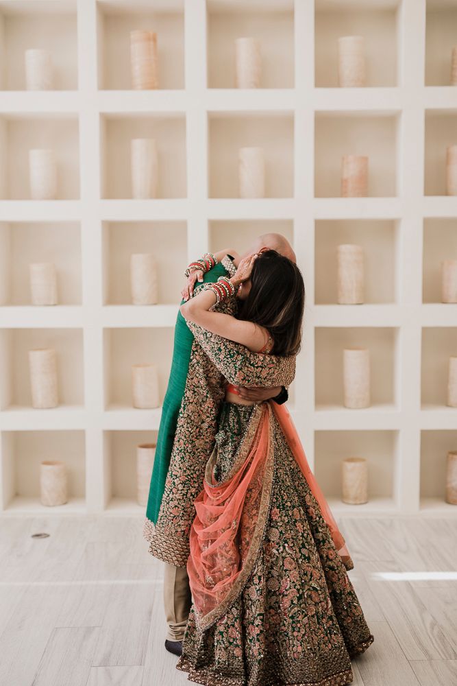 Traditional Indian bridal lehenga in rich brown and gold embroidery with coral dupatta shown in elegant pose.