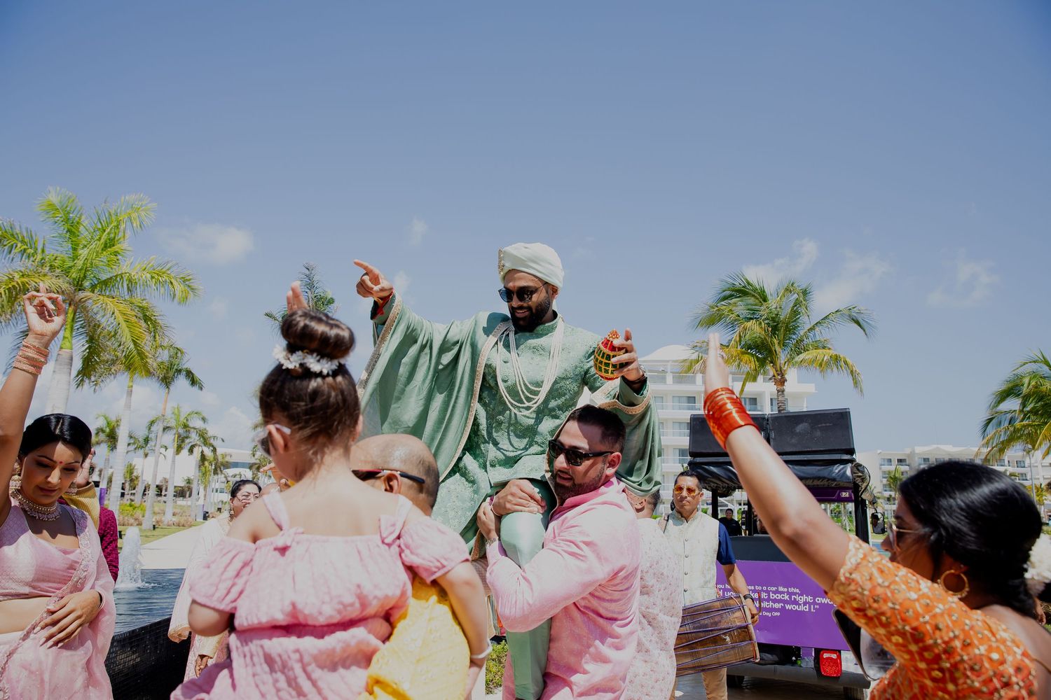 Joyful outdoor wedding celebration with guests dancing under palm trees.