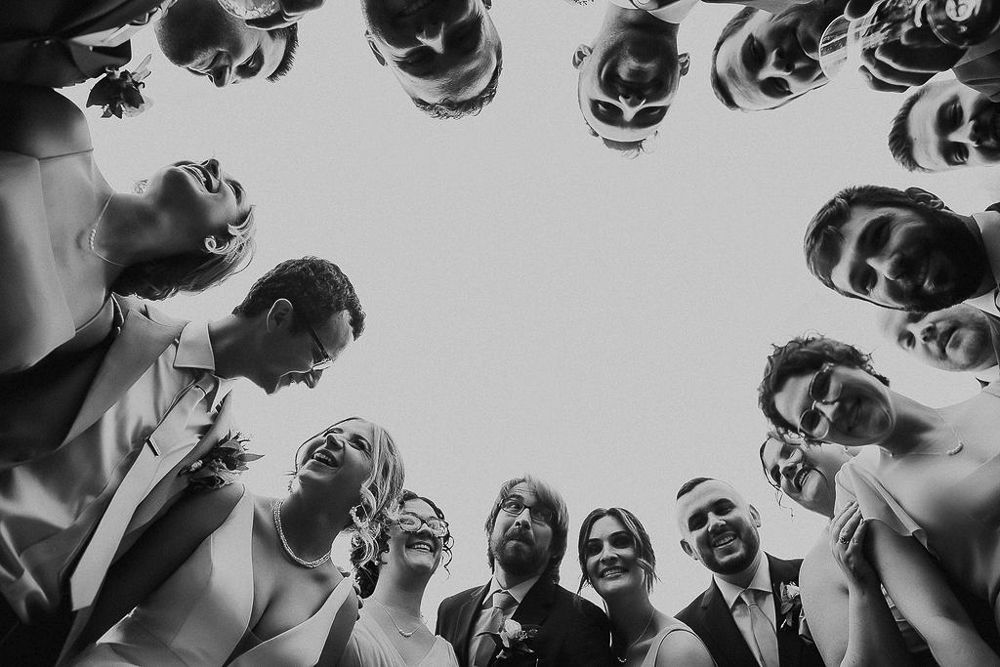 Low angle black and white photo showing a circle of people looking down at the camera with dramatic lighting.