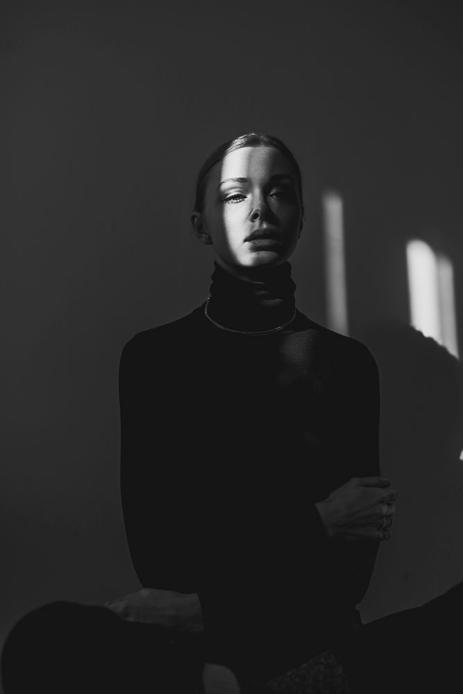Moody black and white portrait with dramatic side lighting creating deep shadows.