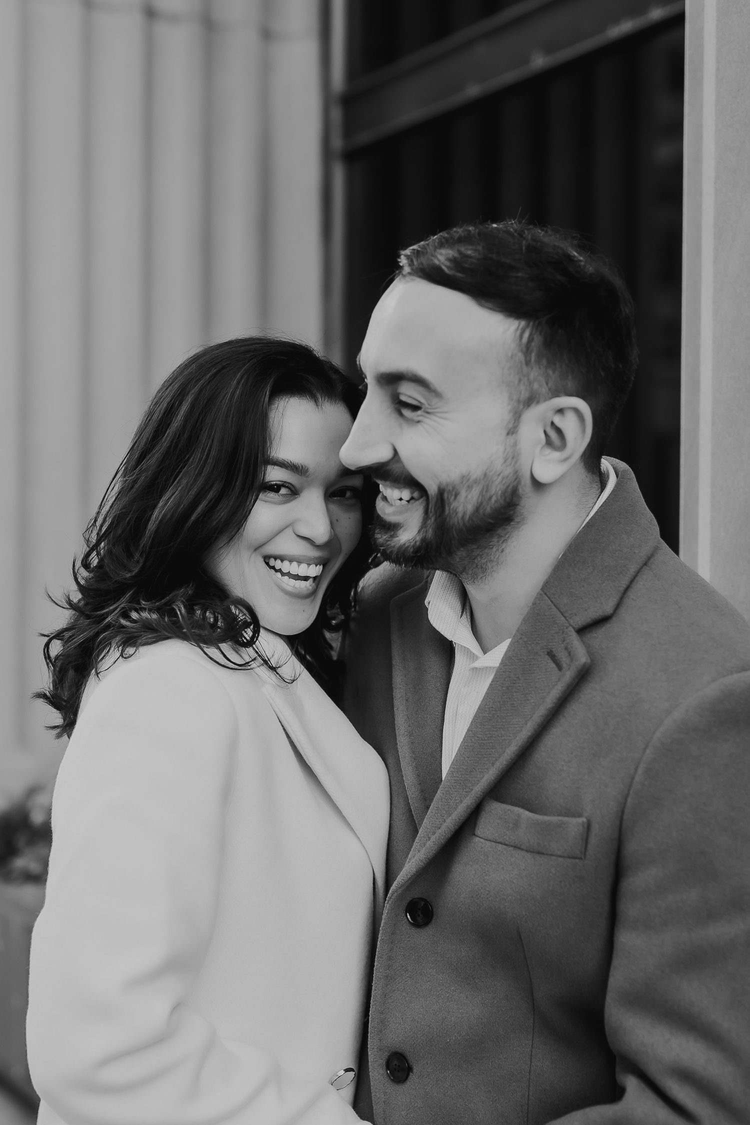 A couple shares an intimate moment laughing together in black and white portrait photography.