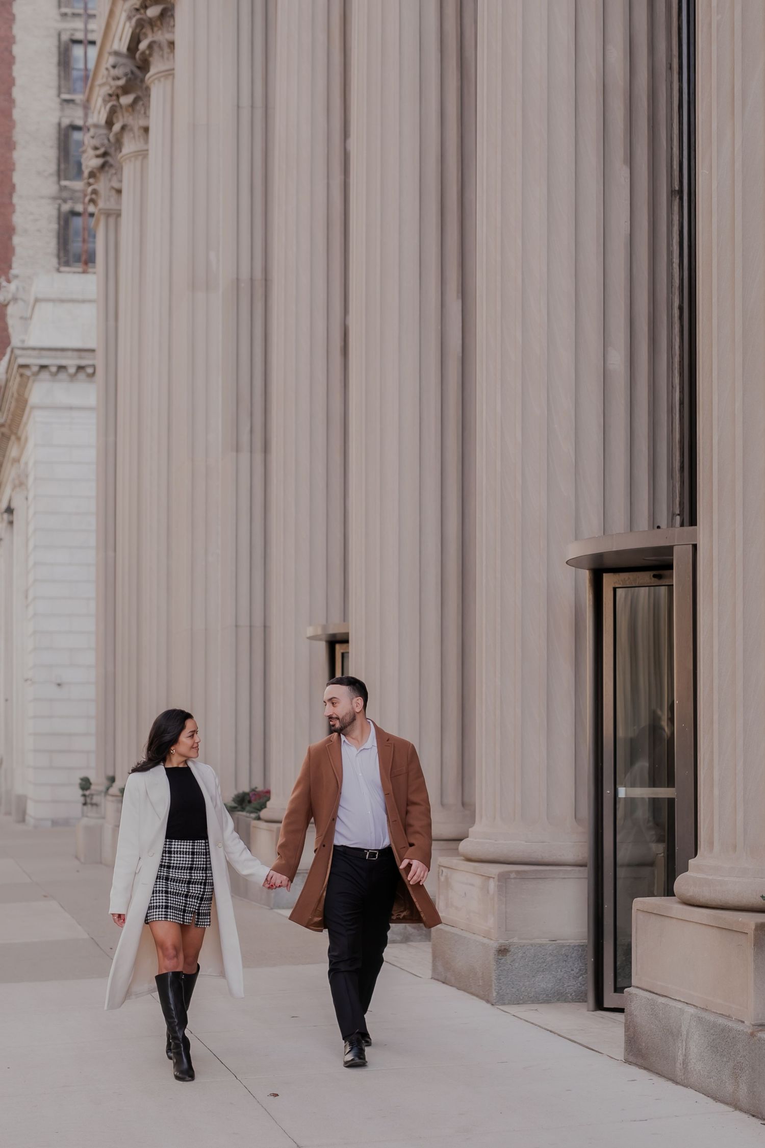 Couple walking past white stone columns and pillars in an elegant architectural setting.