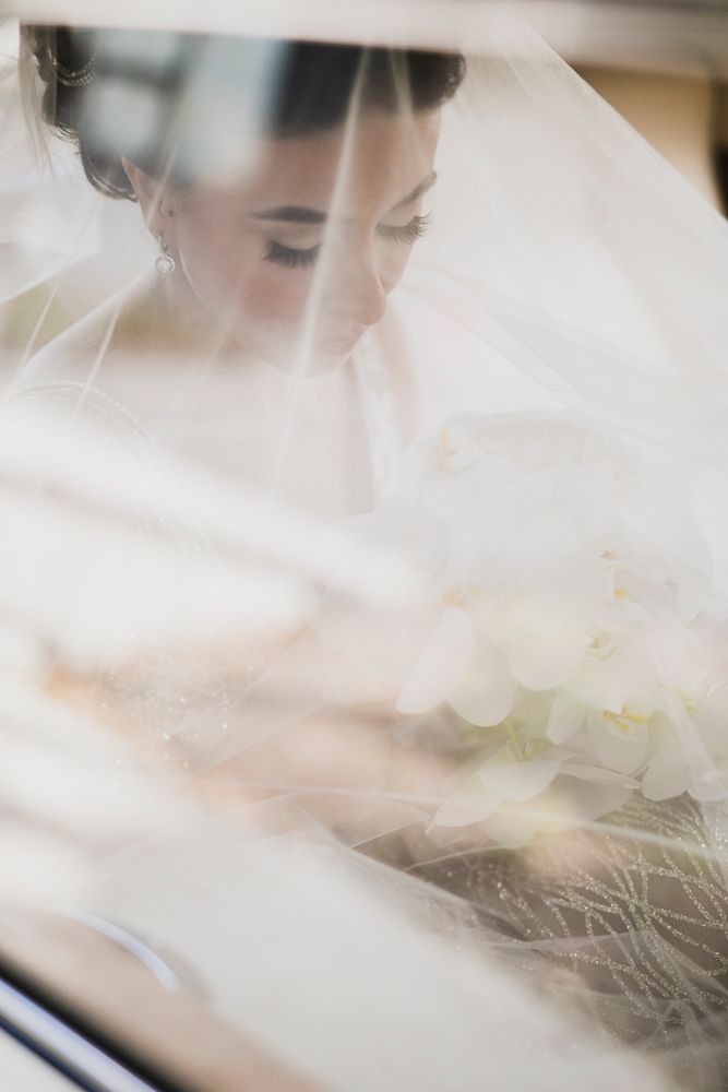 A soft, ethereal bridal portrait through a delicate veil with white flowers in the foreground.