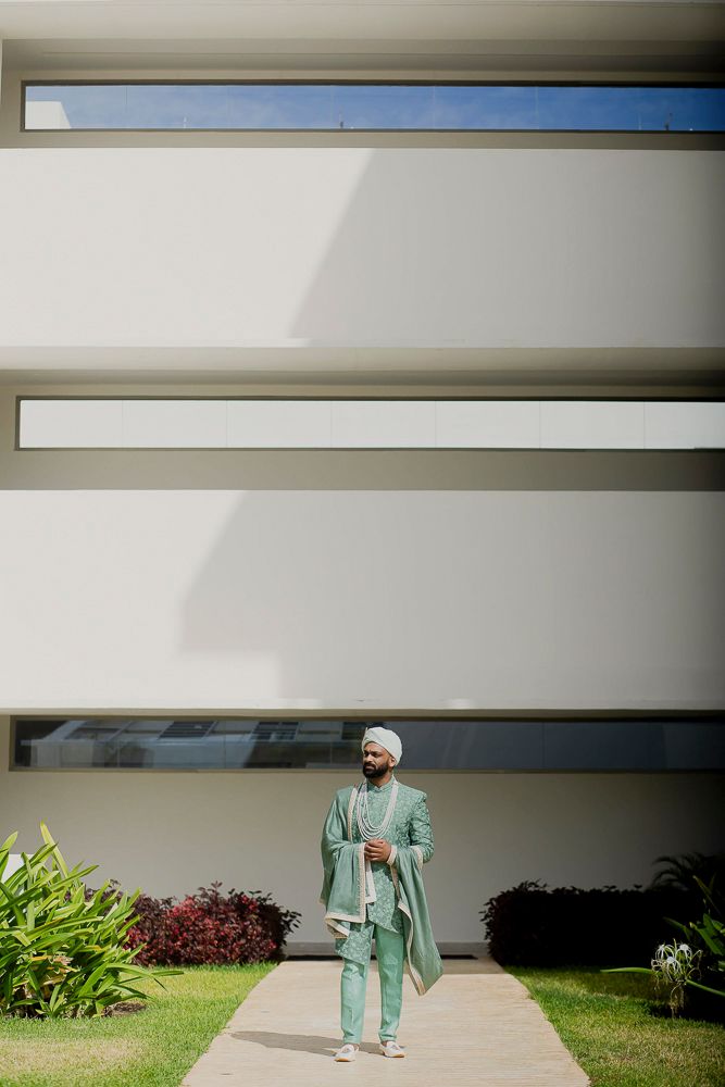 Figure in mint green attire walks along a modern building exterior with white horizontal lines.