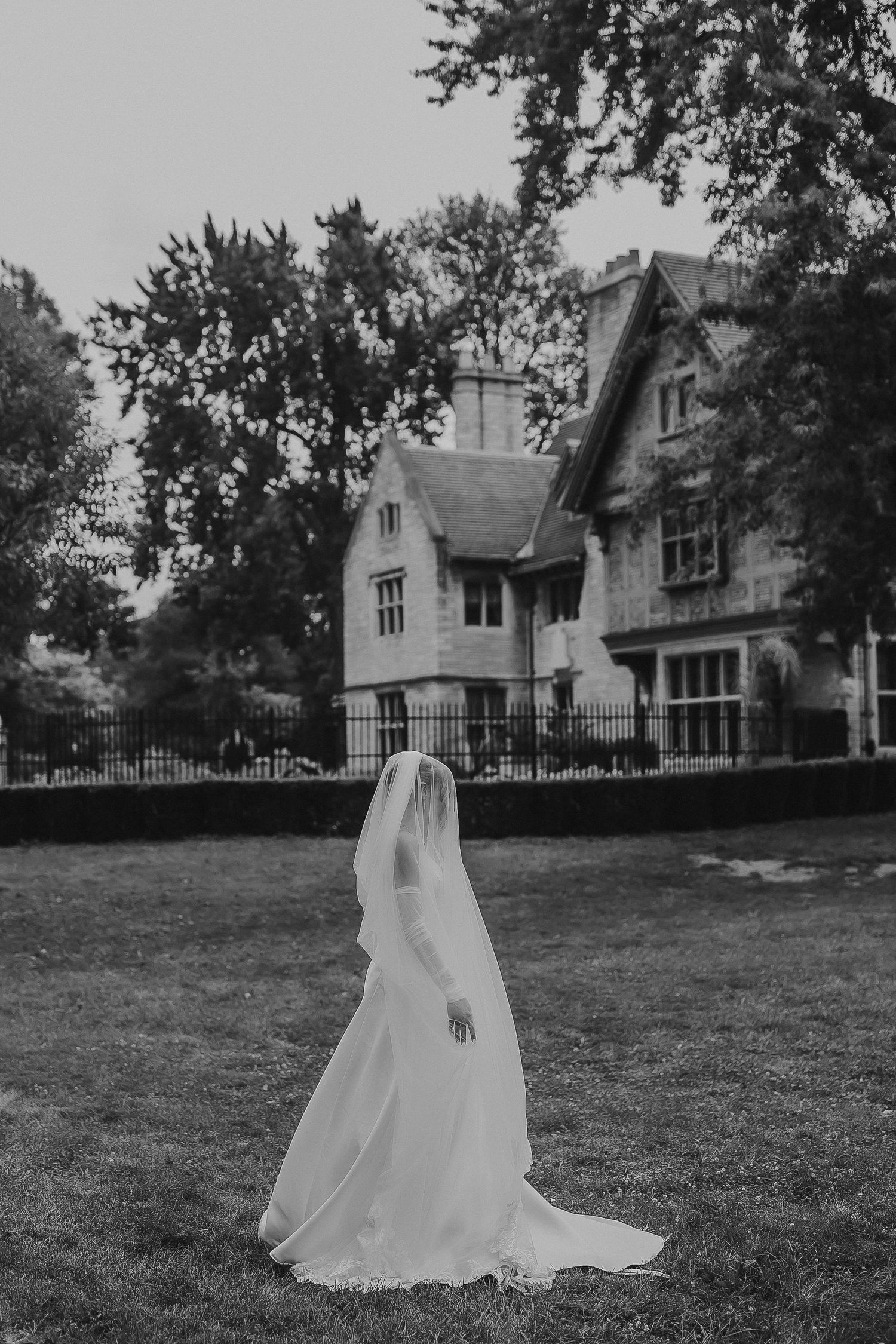 A flowing white wedding dress creates a dramatic silhouette on a mansion lawn.