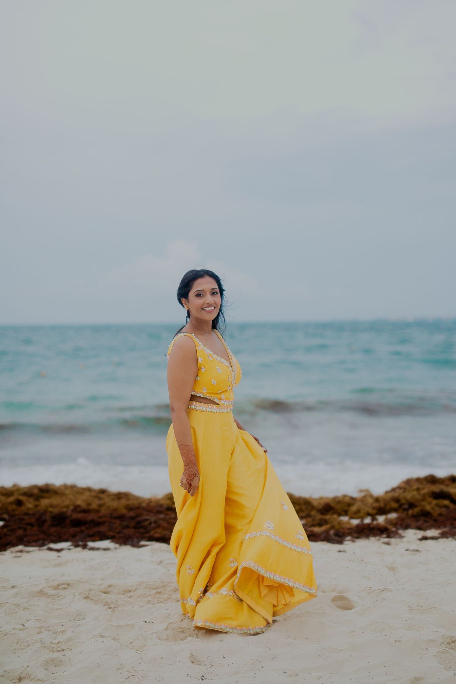 A yellow dress flows in the ocean breeze as someone poses on a beach.