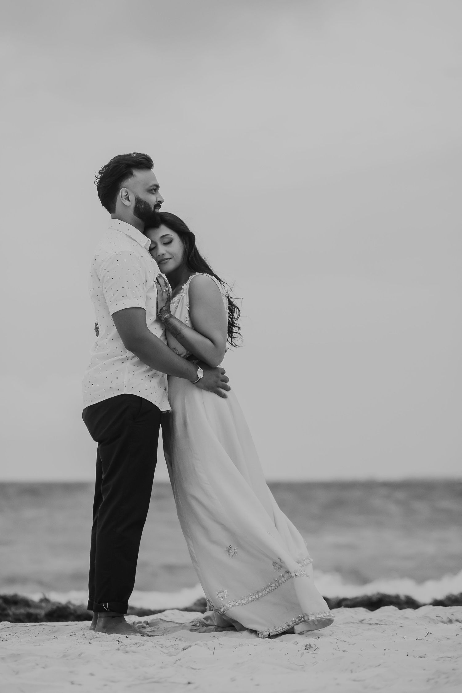 A couple embraces on a beach in black and white photography.