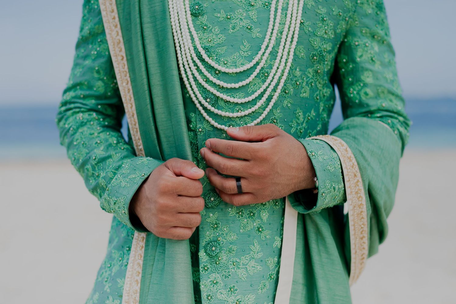 Detail shot of mint green sherwani with pearl necklaces and intricate embroidery.