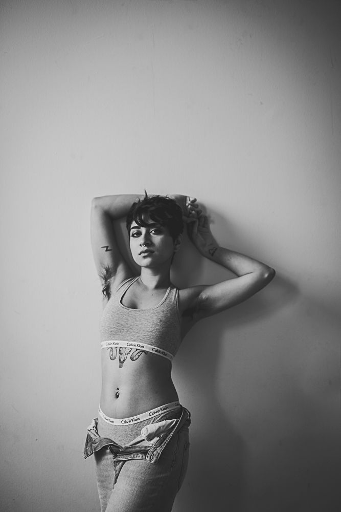 Black and white fashion photo of person in casual attire posing against plain wall with dramatic lighting.