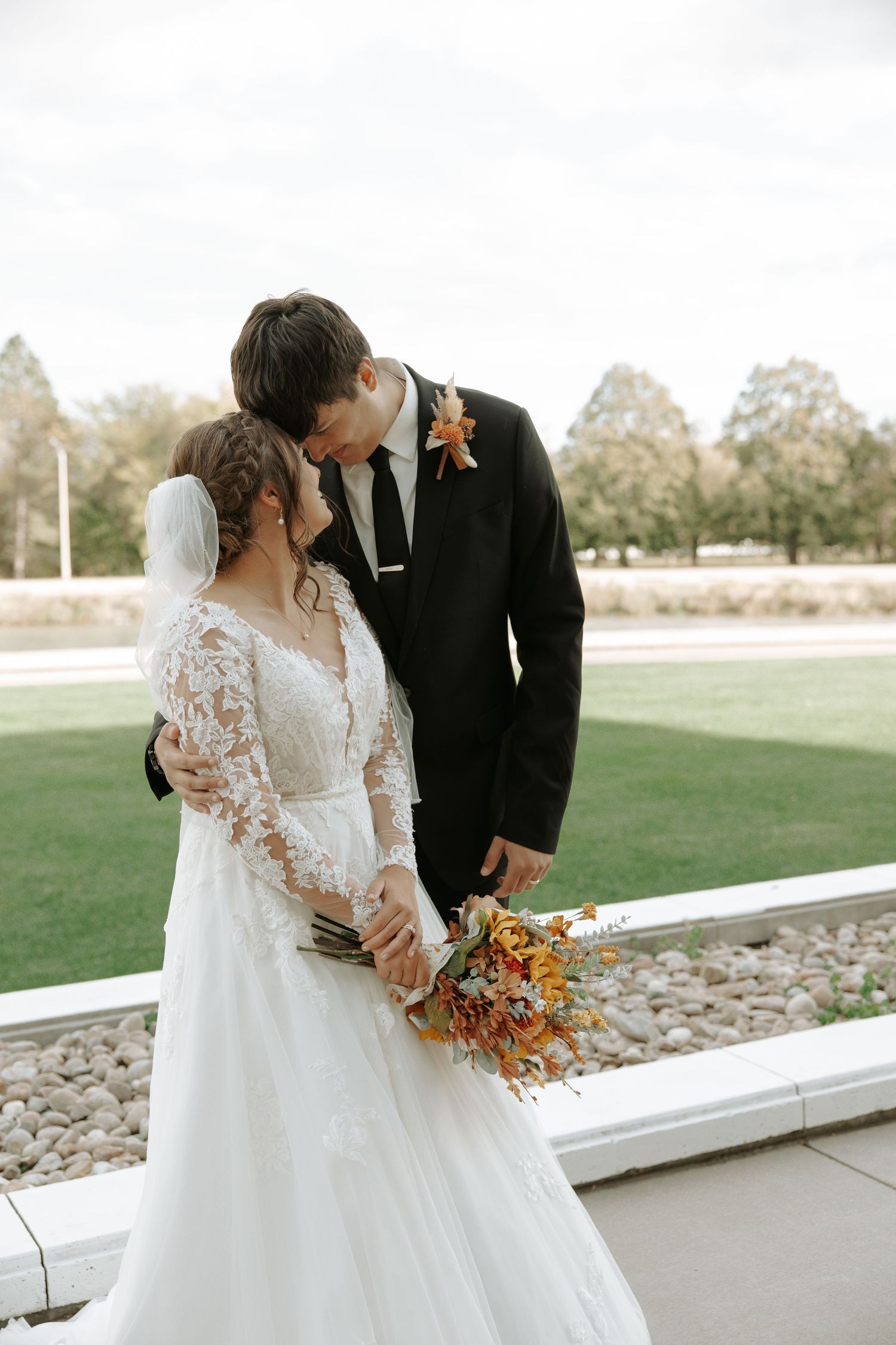 Newlyweds share intimate moment with autumn bouquet against outdoor backdrop.