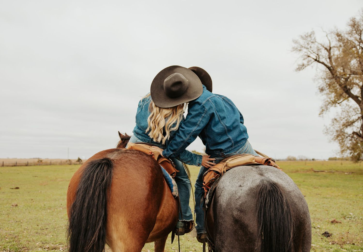 Two horses with riders pause side by side in open pasture.
