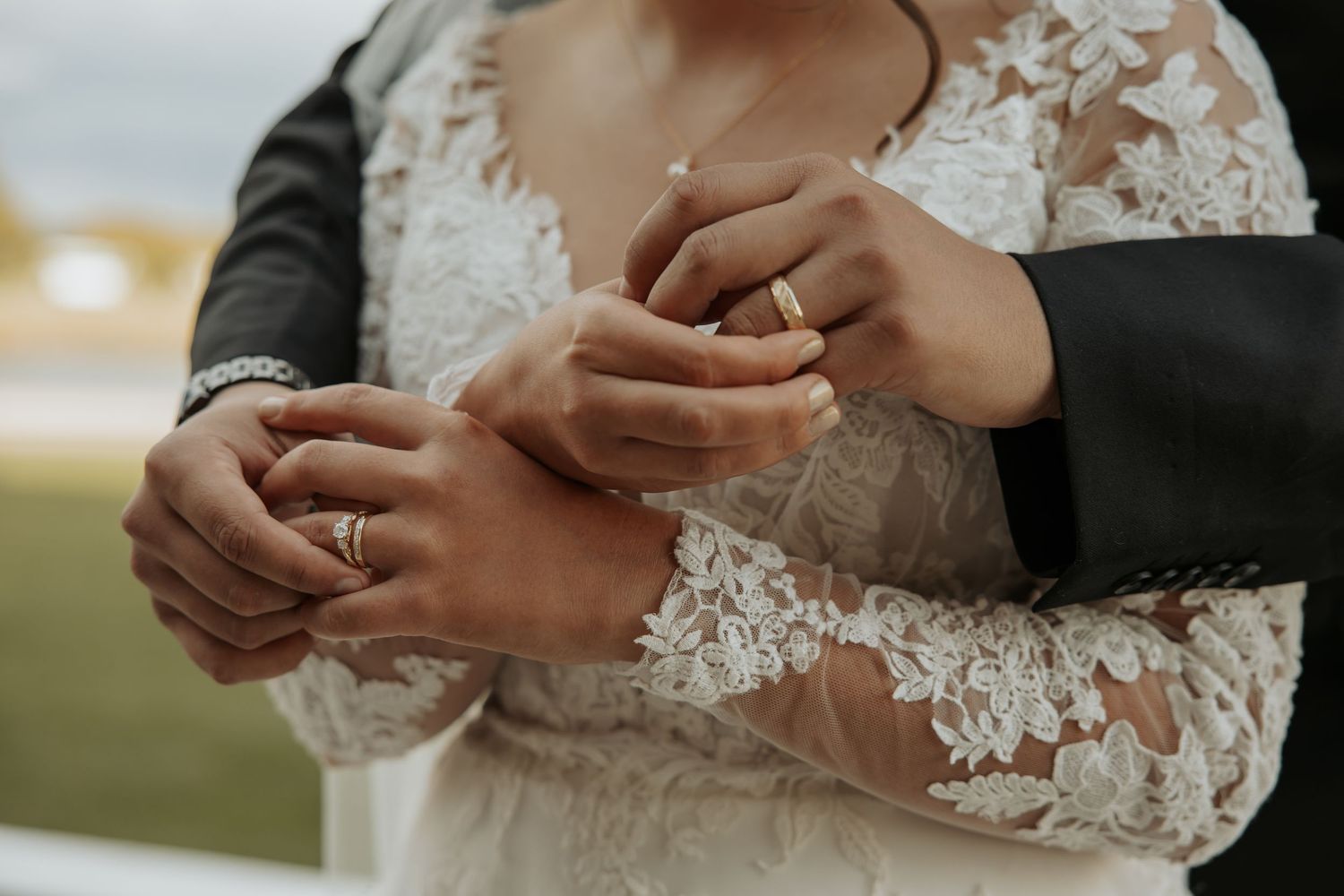 Close up of wedding rings being exchanged with detailed lace sleeves visible.