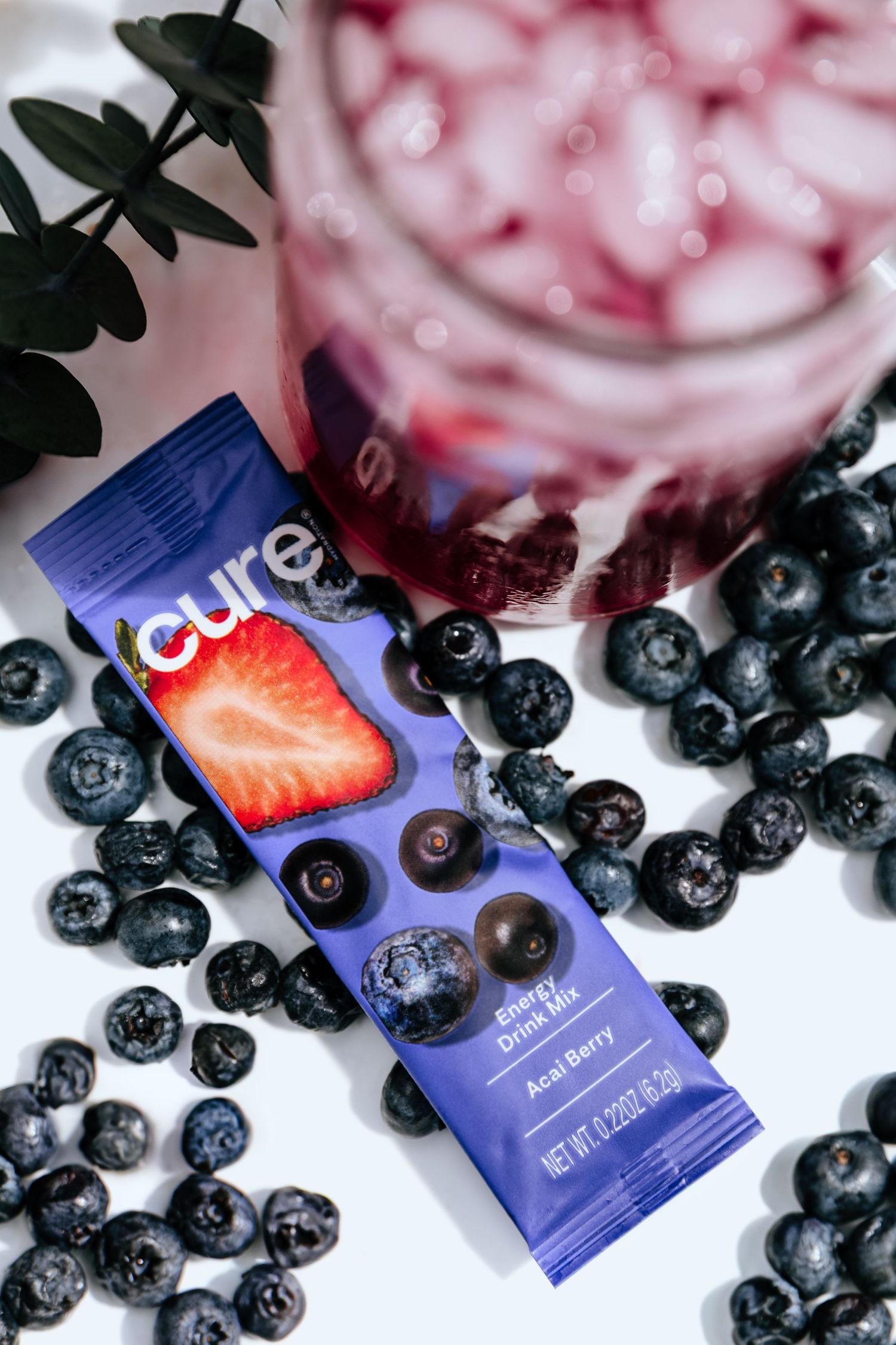 Fresh blueberries scattered around Cure hydration packets and pink iced beverage.