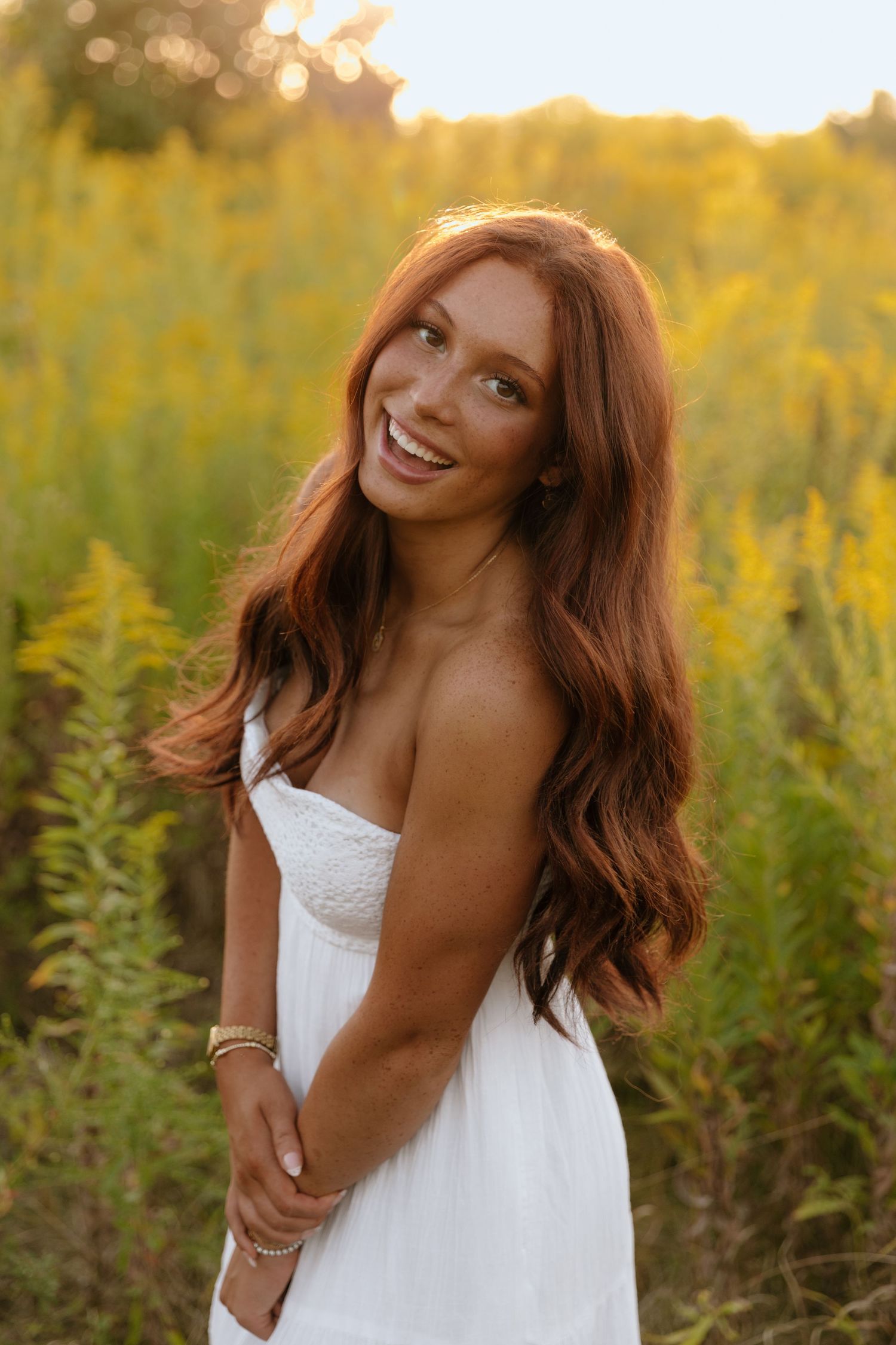 A person in a white dress laughs joyfully in a golden field at sunset.