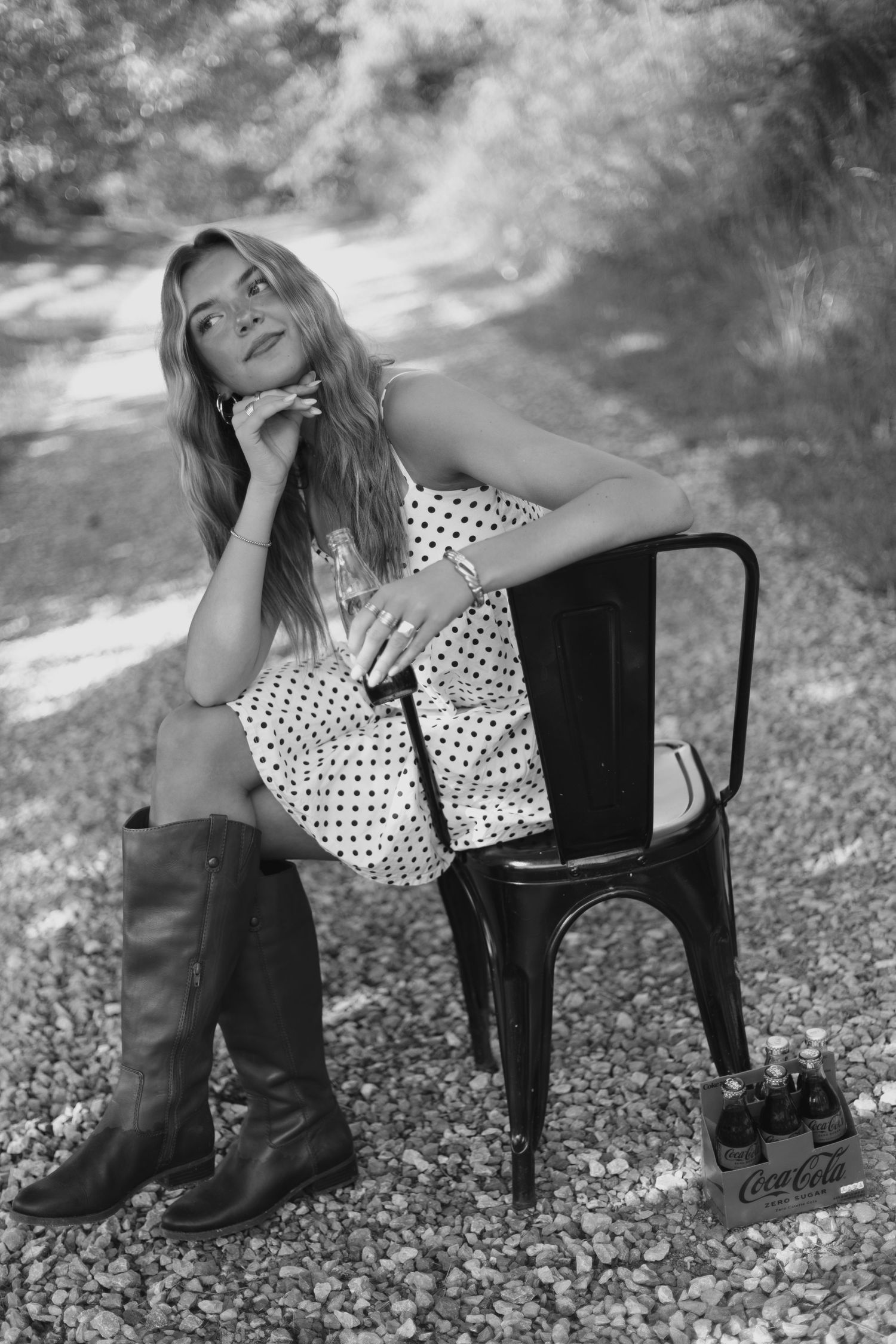 A series of black and white artistic photos showing someone in a polka dot dress and boots lounging on a black chair outdoors.