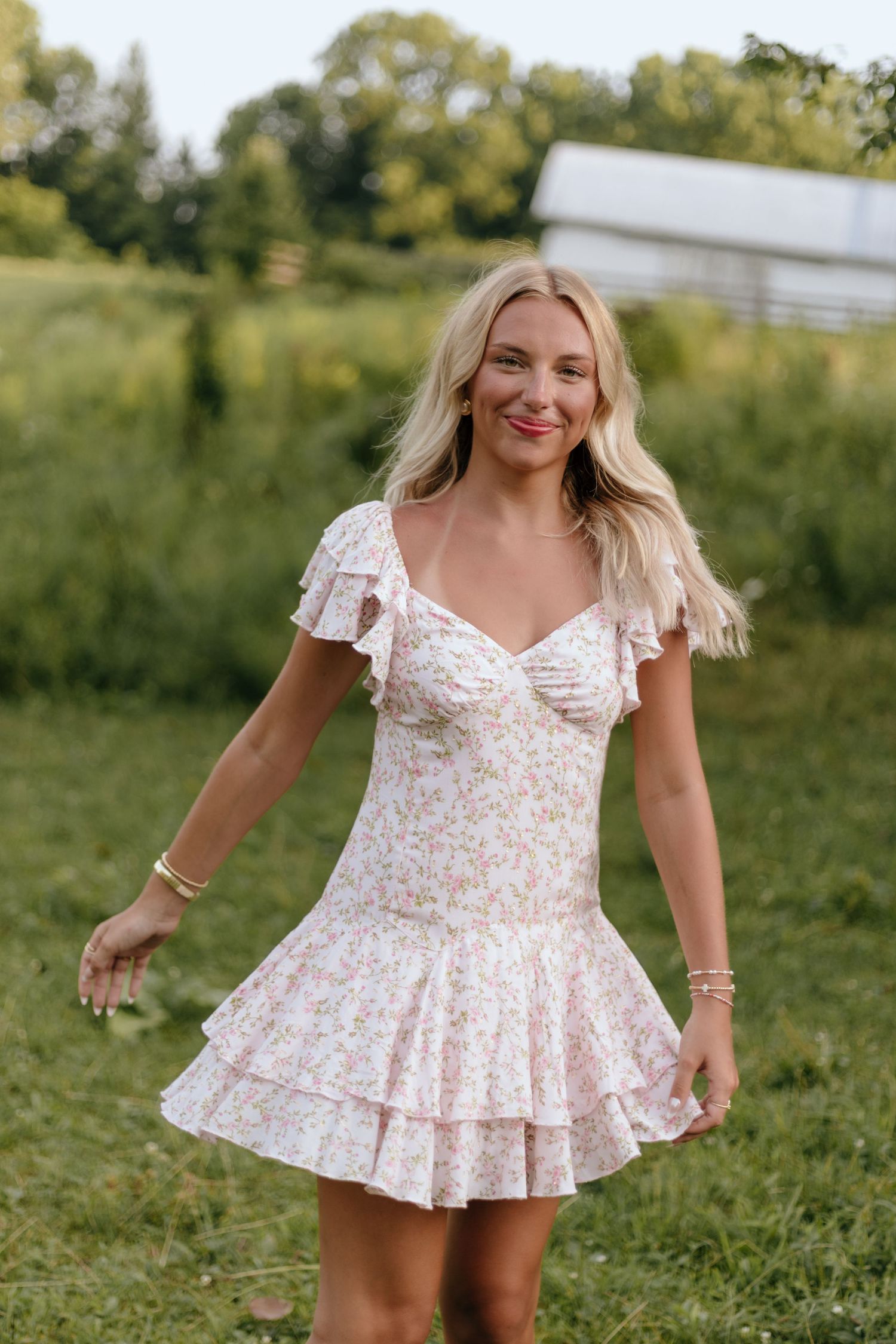 A floral print peplum top with flutter sleeves shown in a sunny outdoor field setting.