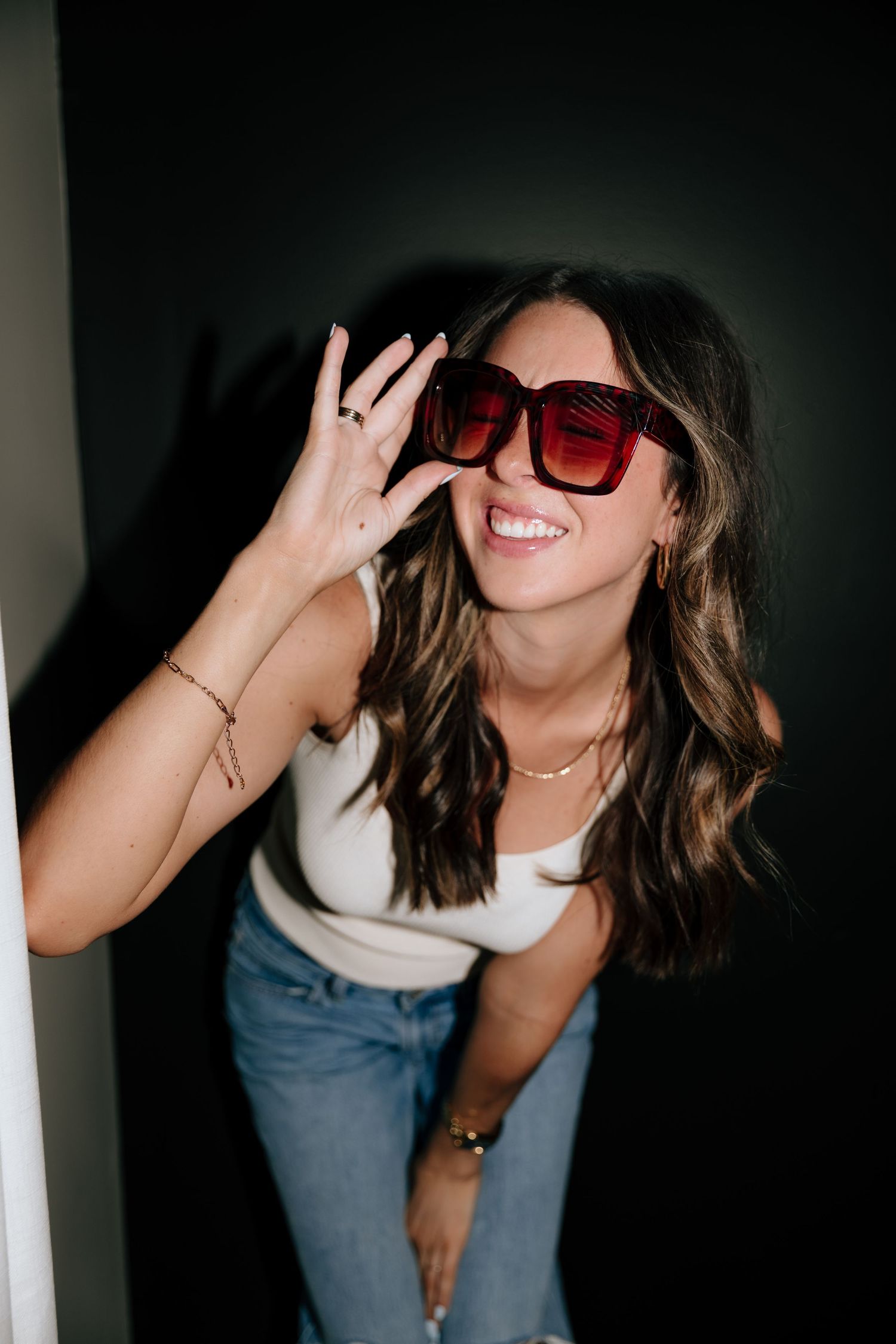 Stylish poses with red sunglasses in dramatic lighting against dark background.