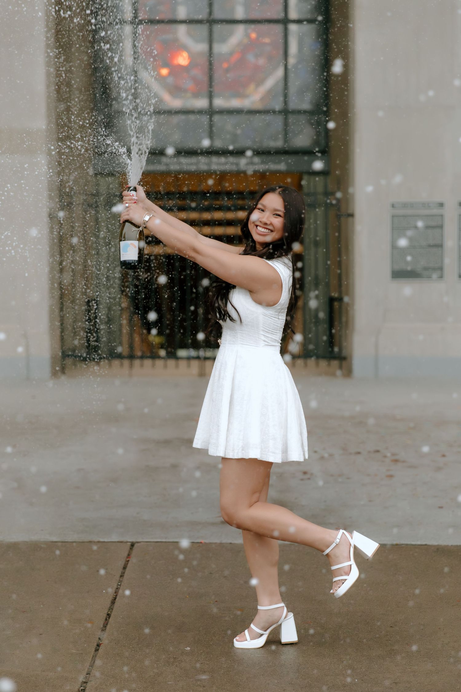 A dancer in a white dress performs graceful movements in front of a building while snow falls around them.