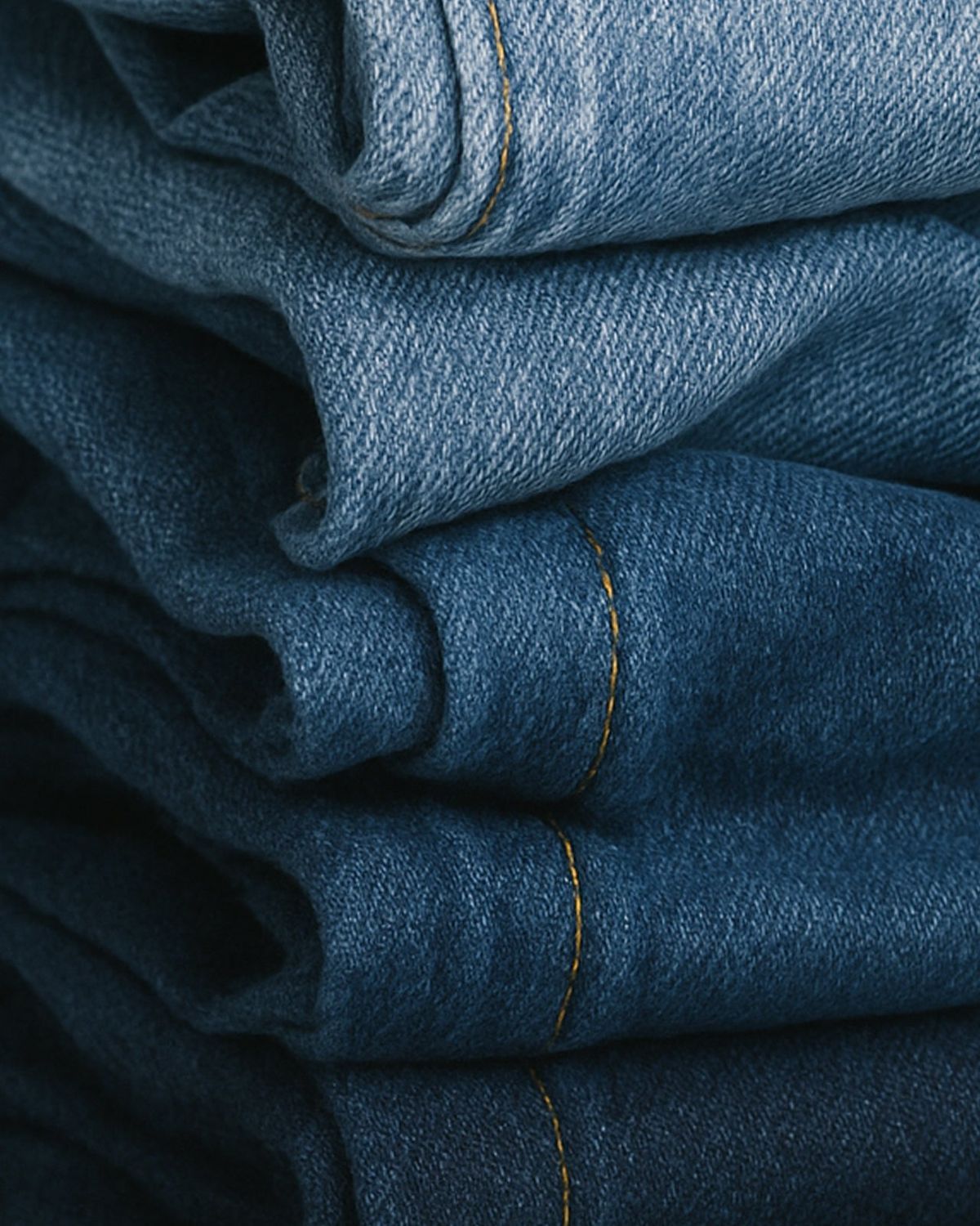 Stack of folded blue denim jeans showing textured fabric and stitching details in close-up view.