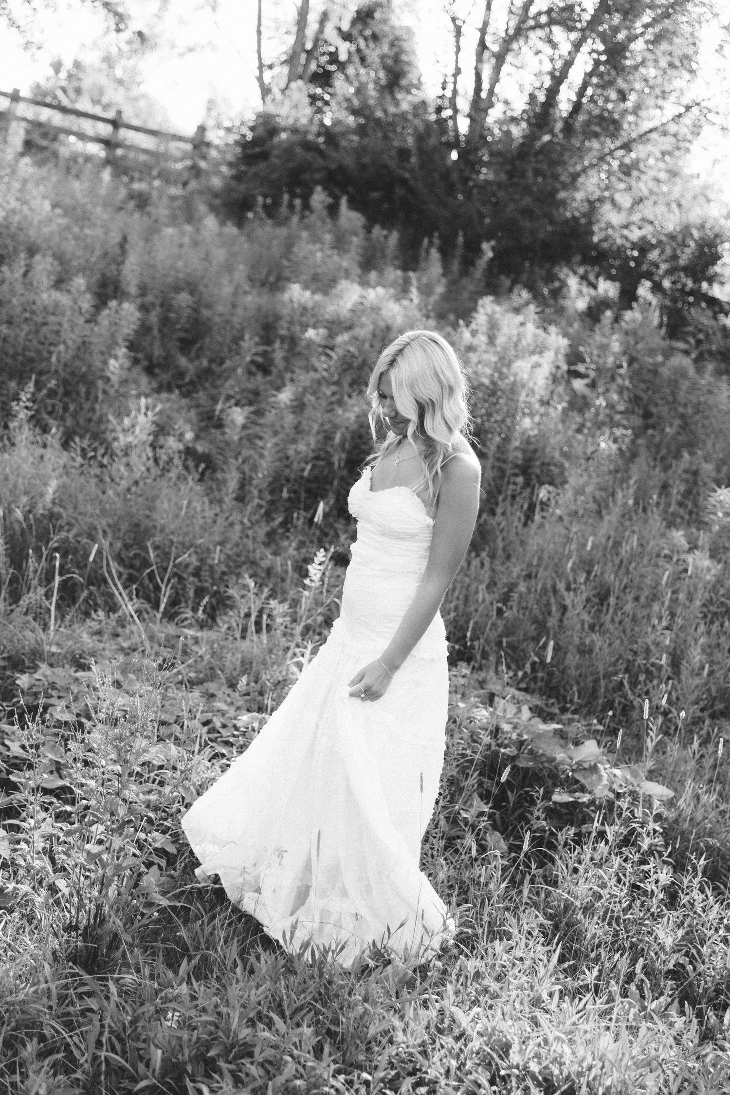 Black and white photo of a bride in a flowing white gown standing in a lush outdoor field.