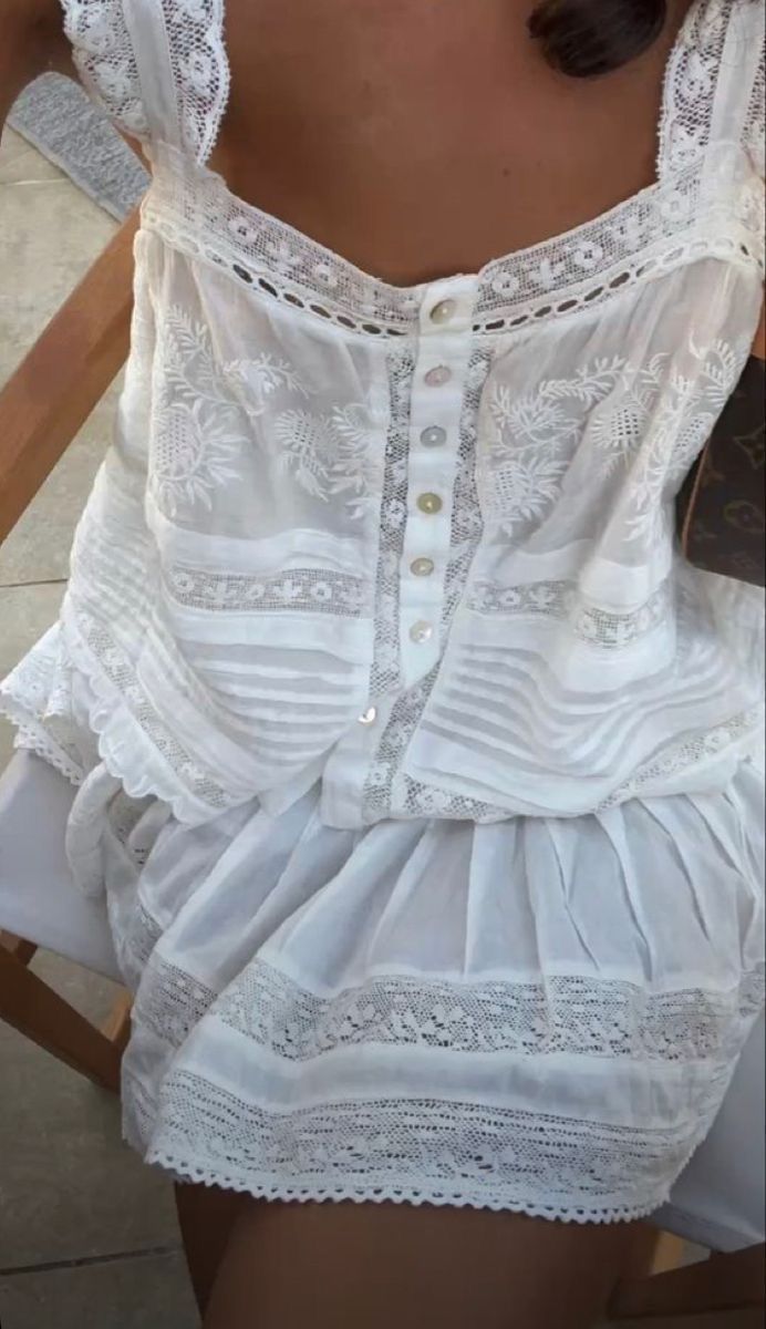 Delicate white lace summer dress with embroidered details, buttons and ruffled tiers features intricate floral patterns.
