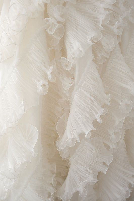 Delicate white ruffled tulle fabric with intricate pleats and layers creates an ethereal bridal texture.