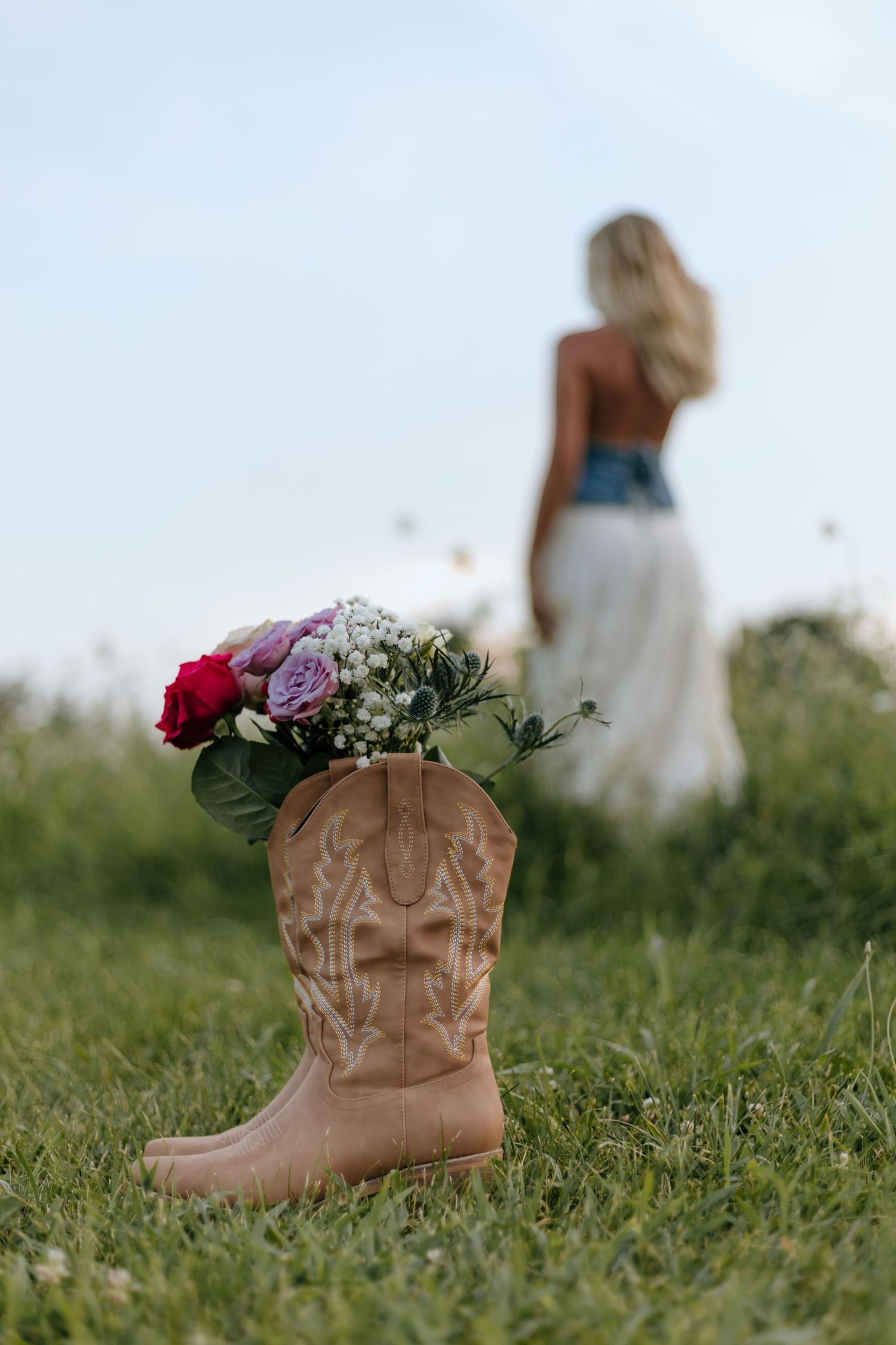 Brown leather cowboy boots filled with colorful flowers sitting in green grass.