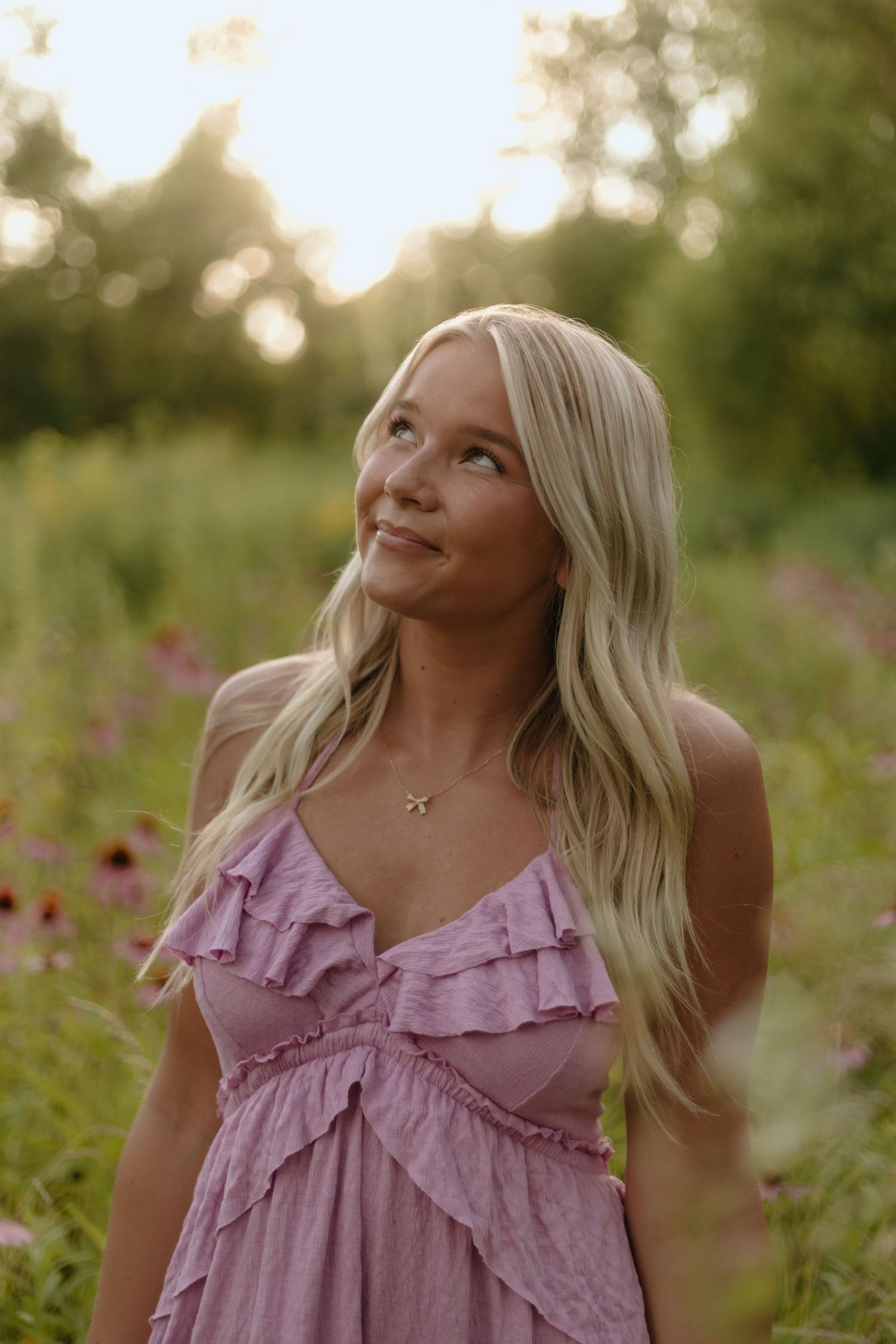 A person in a pink ruffled top poses thoughtfully in a wildflower field during golden hour.