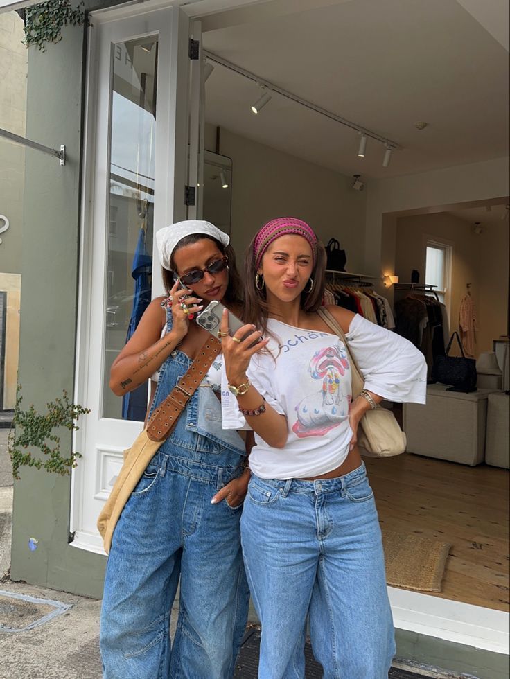 Two stylish women pose for a selfie outside a boutique shop, wearing denim outfits and colorful headbands.