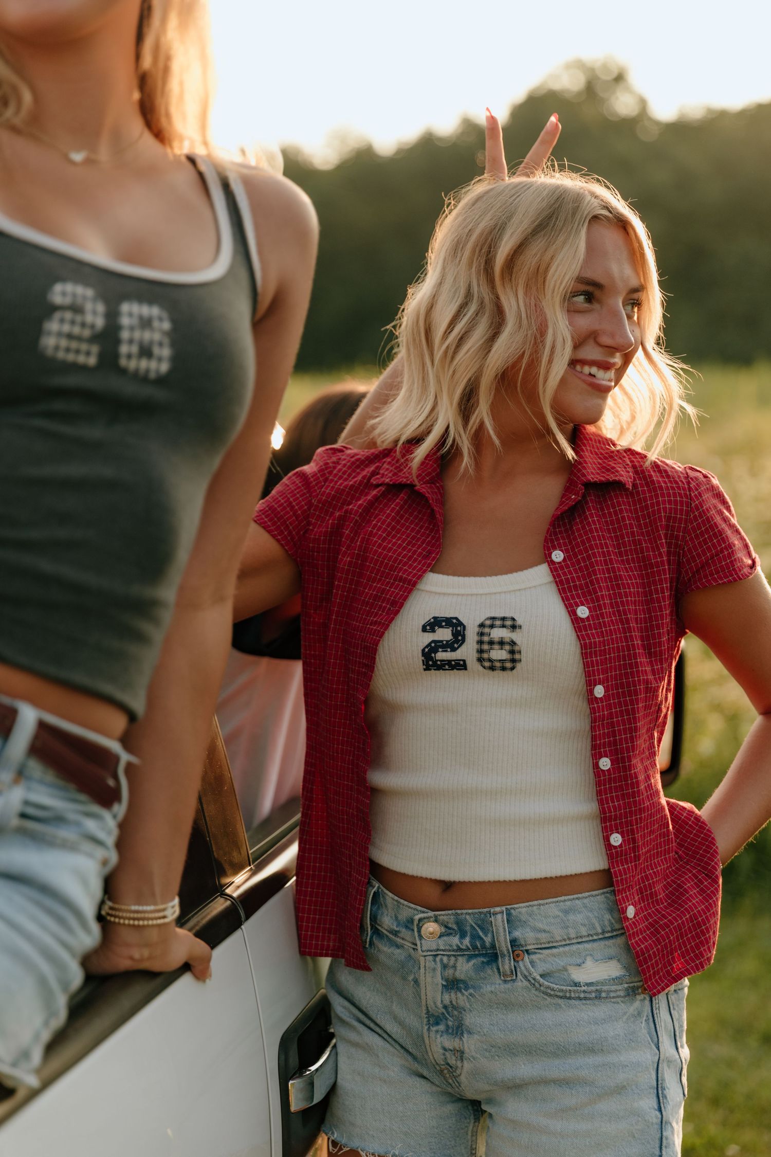 Person wearing red plaid shirt and jeans poses outdoors at sunset in casual summer style.