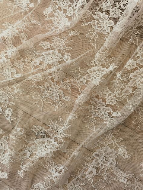 Delicate floral lace fabric in cream color with intricate embroidered patterns creating a romantic texture.