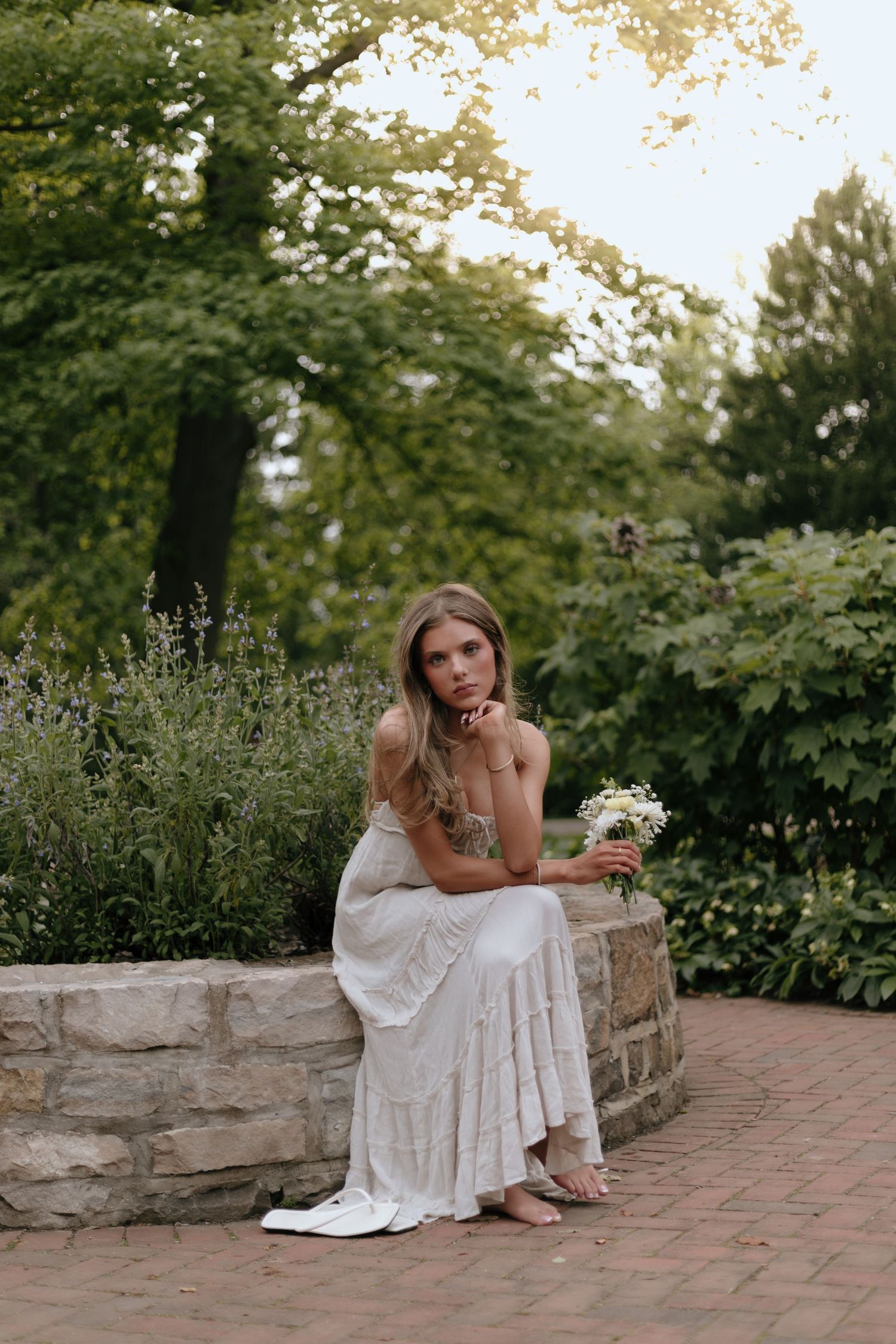 Romantic garden portrait with white dress against lush greenery and stone wall.