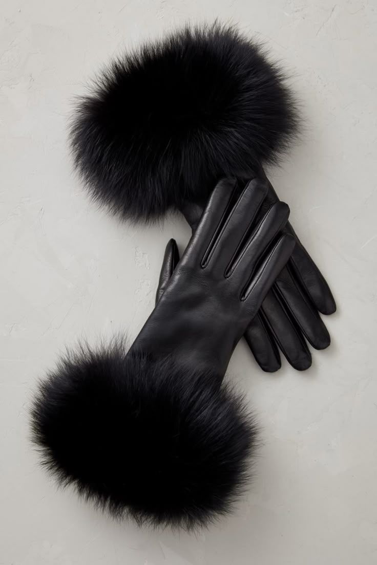 Elegant black leather gloves with luxurious fur pom pom accessories arranged on white background.