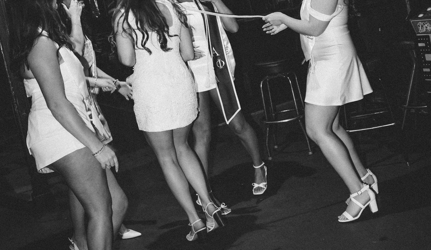 Black and white photo of women in white mini dresses dancing at a party or nightclub event.