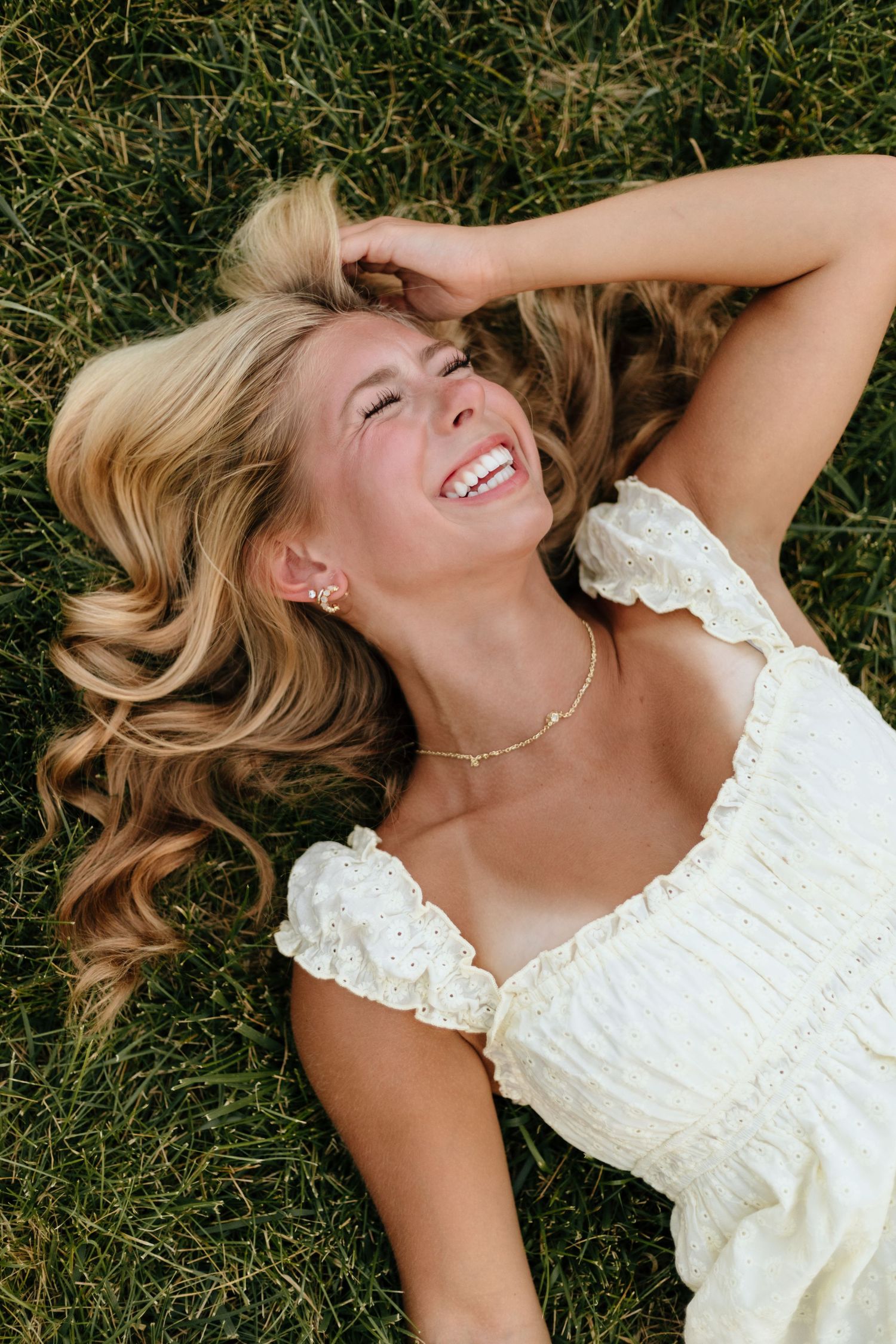 Person in white lace dress lying on grass during summer photoshoot.