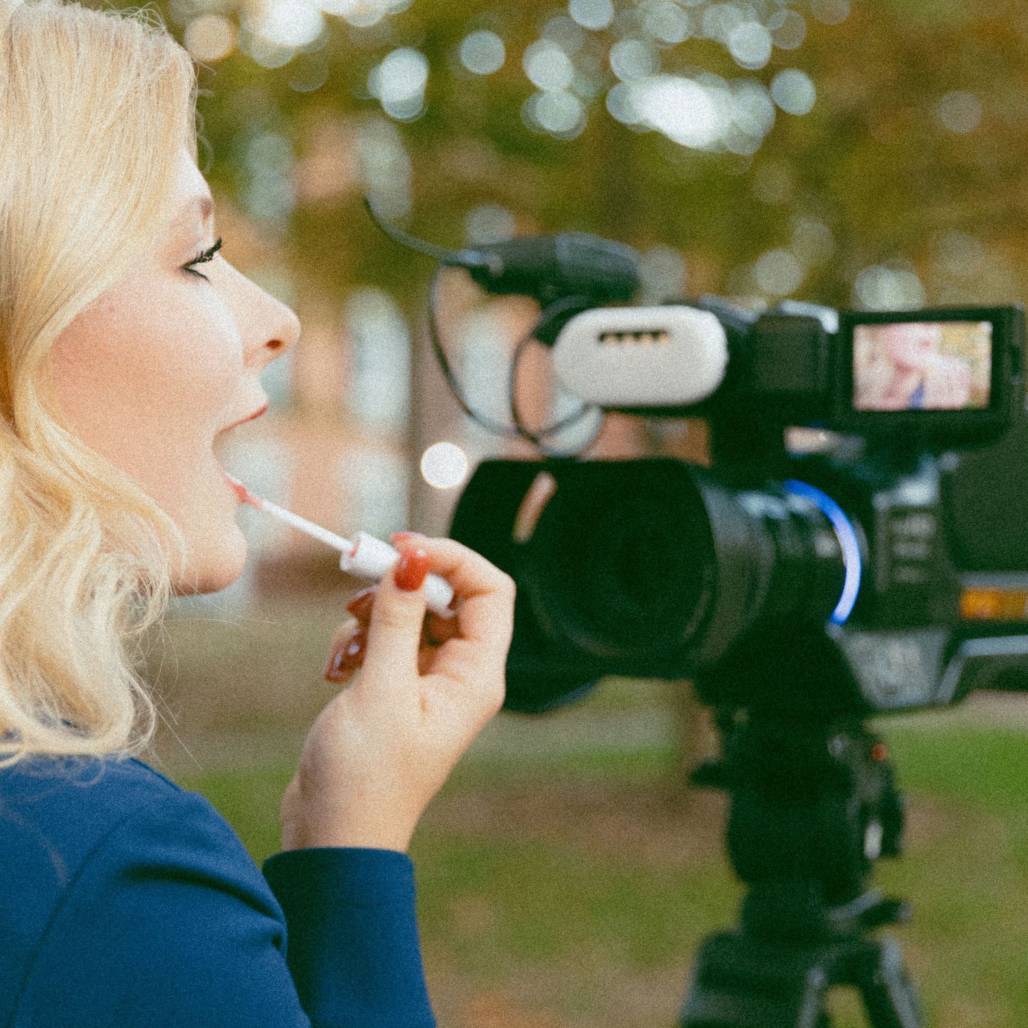 Behind the scenes shot of someone getting makeup applied while being filmed with a professional video camera outdoors.
